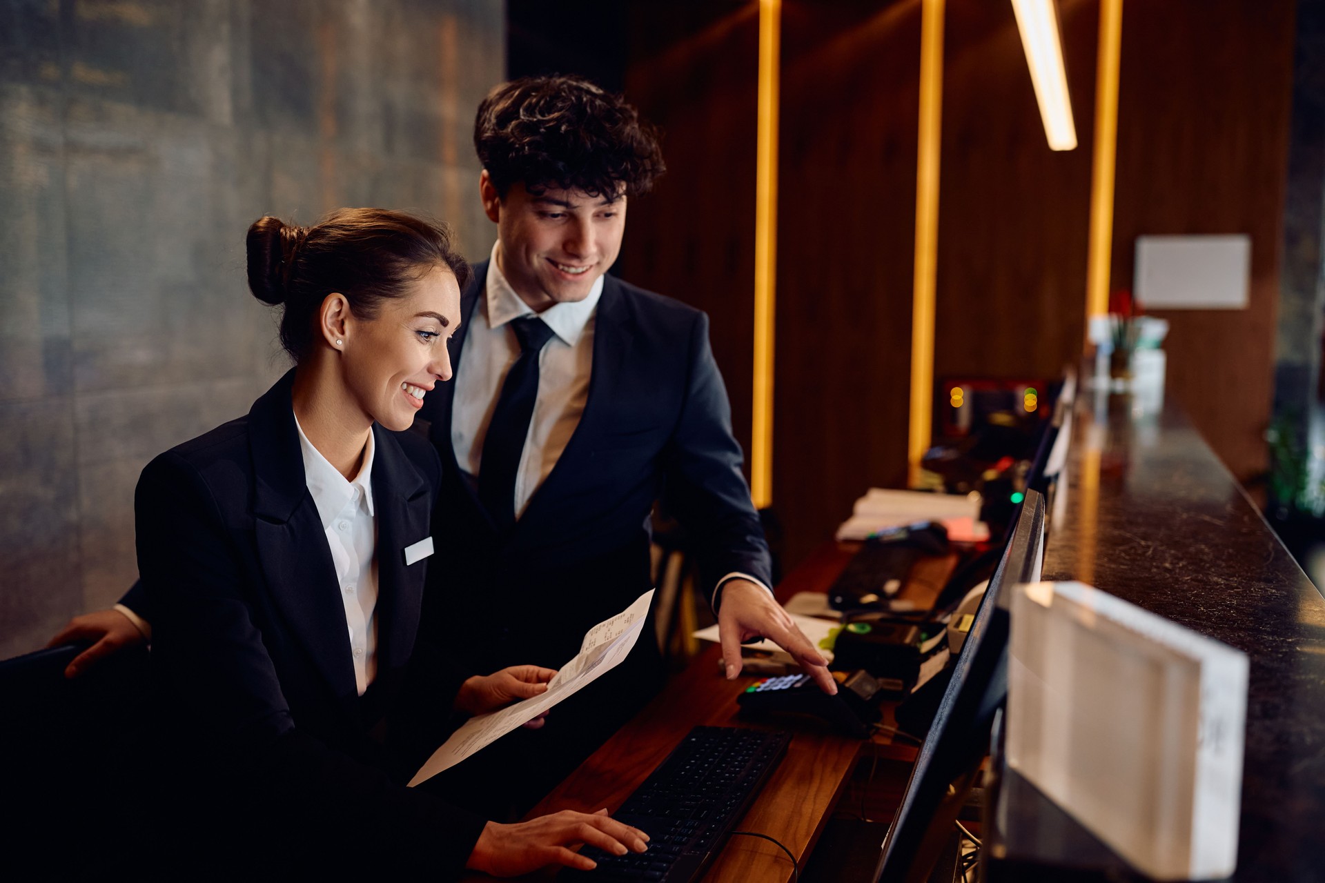 Happy receptionists cooperating while working on a computer at hotel front desk. Happy receptionists cooperating while working on a computer at hotel front desk.